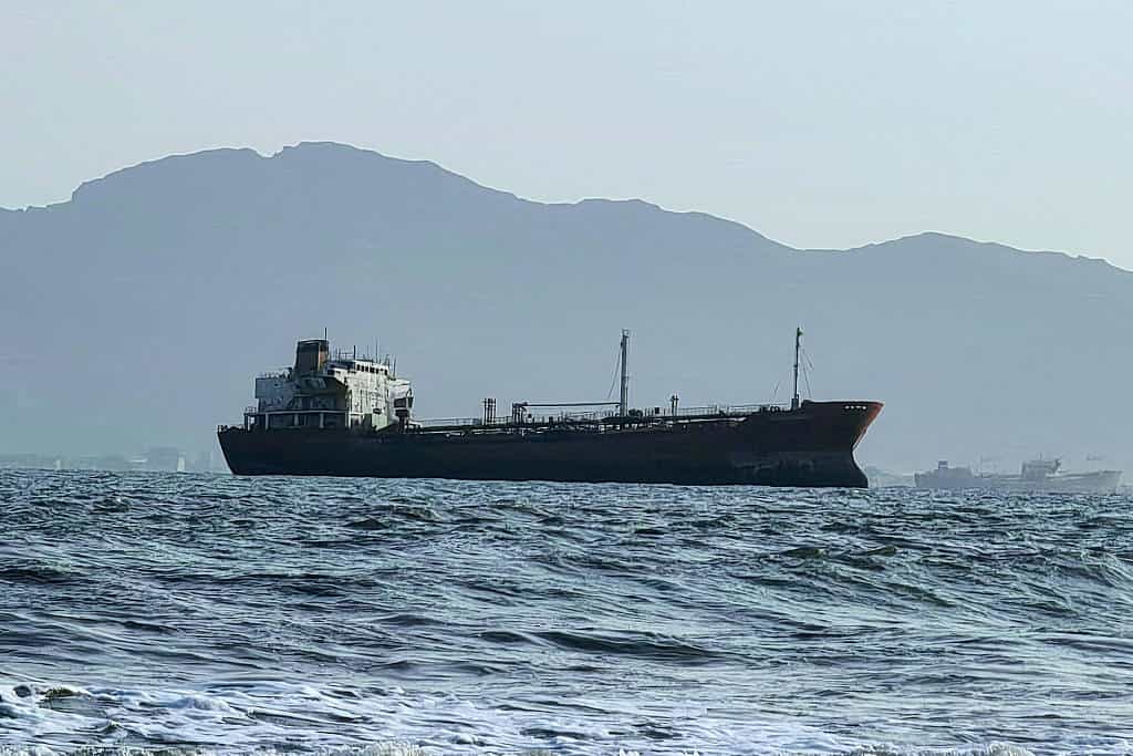 Navio mercante navegando, oceano calmo com montanhas ao fundo.