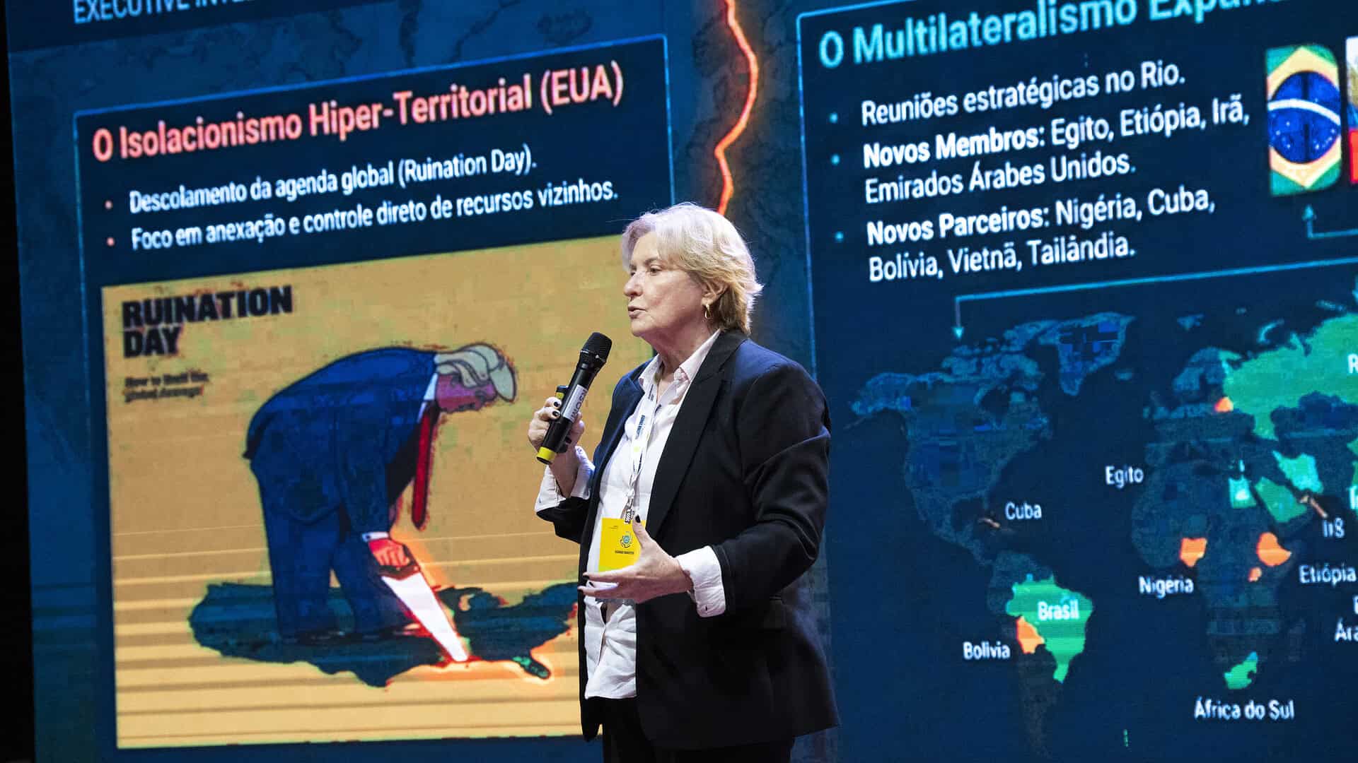 Palestra com apresentador em palco e tela com mapas.